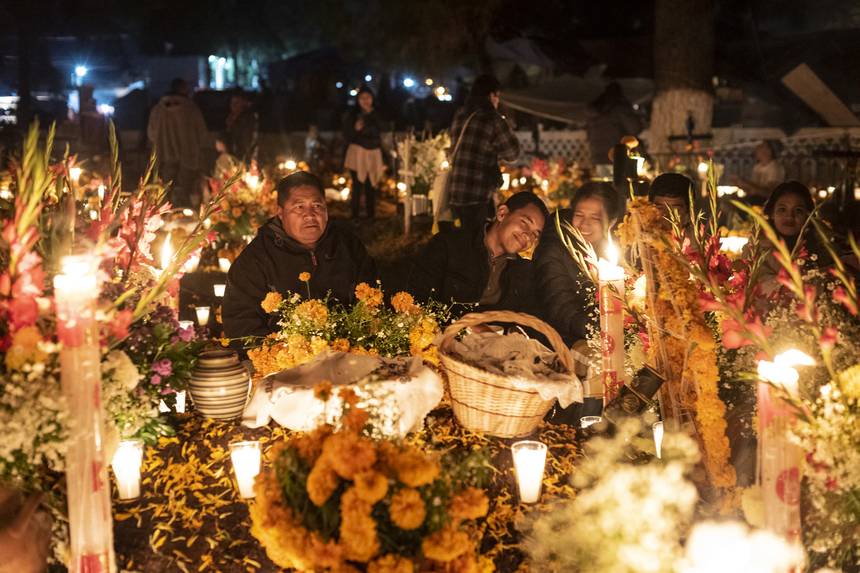 A family keeping vigil at a candlelit grave banked with marigolds and gladioli